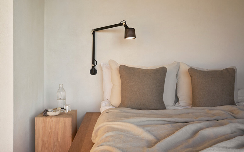 Schlichtes Schlafzimmer mit Doppelbett, zwei grauen Kissen, Holznachttisch und schwarzer Wandlampe.