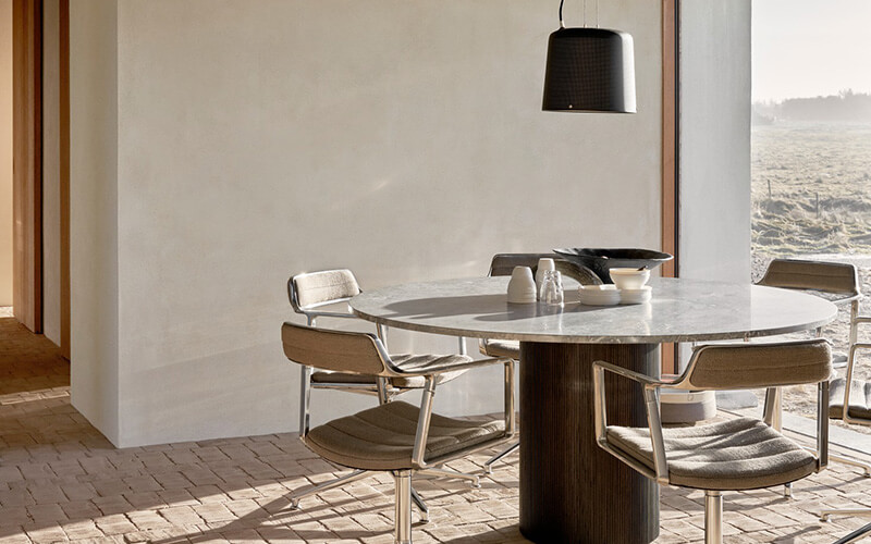 Moderner runder Esstisch mit Marmorplatte und vier Holzstühlen in hellem Raum mit großem Fenster und Blick ins Freie.