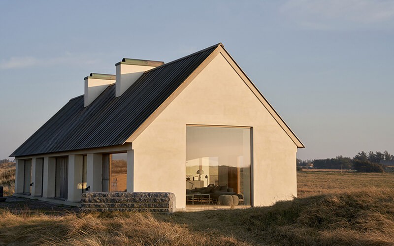 Modernes Ferienhaus mit spitzem Satteldach und großen Fenstern in einer offenen Landschaft mit Gras.