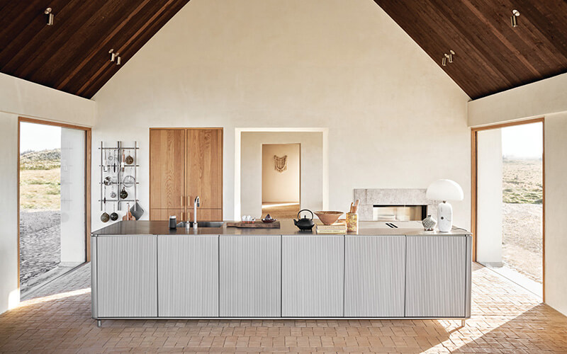 Moderner Küchenraum mit großer Kücheninsel, Holzdecke und zwei großen Fenstern mit Blick auf die Landschaft.