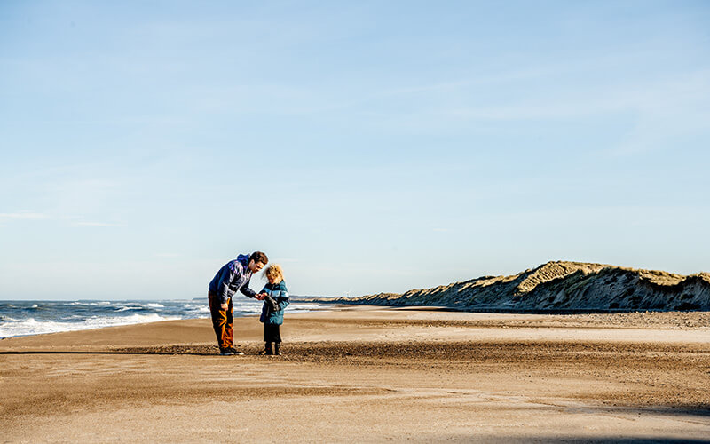 Vater und Sohn stehen am Strand und begutachten ein gesammeltes Fundstück.