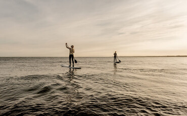Zwei Personen paddeln in der Dämmerung auf SUP-Boards auf dem Wasser.