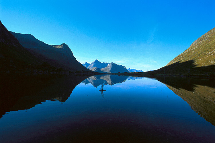 Spiegelglatter Fjord mit Bergsilhouetten im Hintergrund und einem Spritzer auf dem Wasser.