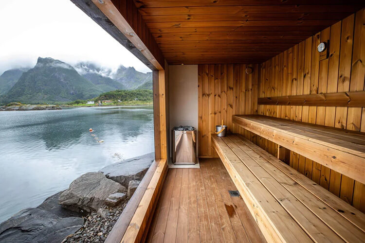 Holzsauna mit mehrstufigen Sitzbänken und Blick auf einen Fjord mit Bergen und Wasser.