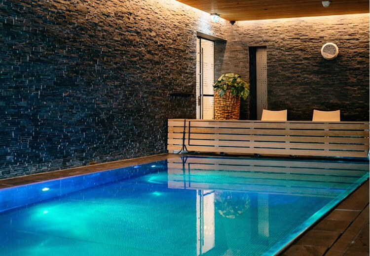 Moderner Innenpool mit blau beleuchtetem Wasser, Holzbank und dunkler Steinwand im Hotel.