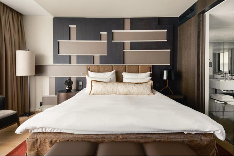 Modern eingerichtetes Hotelzimmer mit großem Bett, zwei Nachttischen, Stehlampe und geometrischer Wanddekoration.