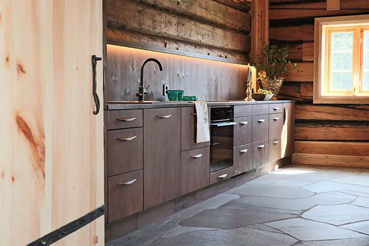 Moderne Küchenzeile mit Spüle, Backofen und Schubladen in einem Raum mit rustikalen Holzwänden und Steinboden.
