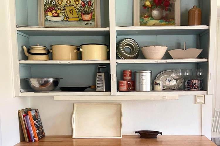 Offene Küchenregale mit Töpfen, Schüsseln, Gewürzdosen, Gläsern und Kochbüchern über einer Holzarbeitsfläche mit einem Tablett und einer kleinen Schale