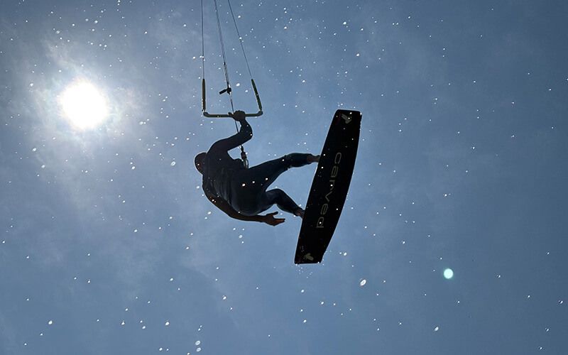 Kitesurfer in der Luft vor hellem Himmel mit Sonne.