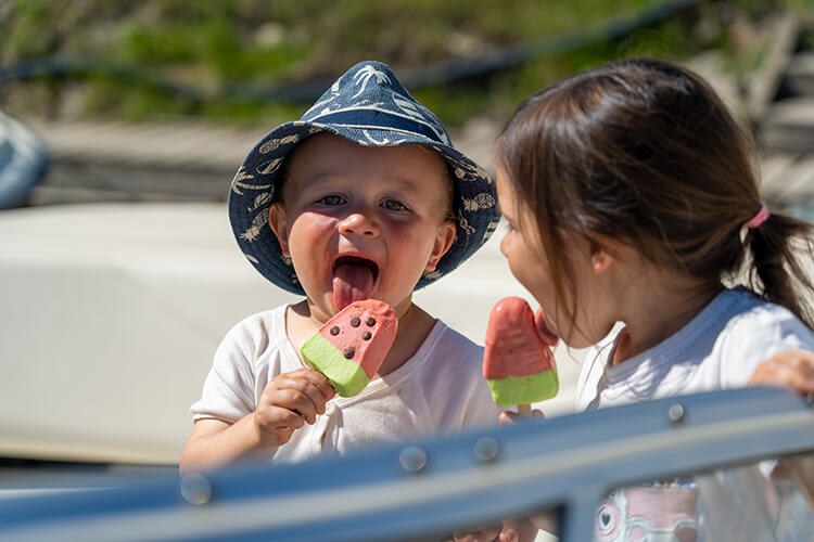 Zwei Kinder sitzen draußen und essen Wassermelonen-Eis am Stiel.