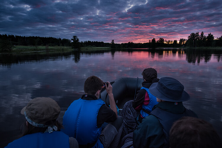 Vier Personen in einem Boot auf einem ruhigen See bei Sonnenuntergang mit bewölktem Himmel