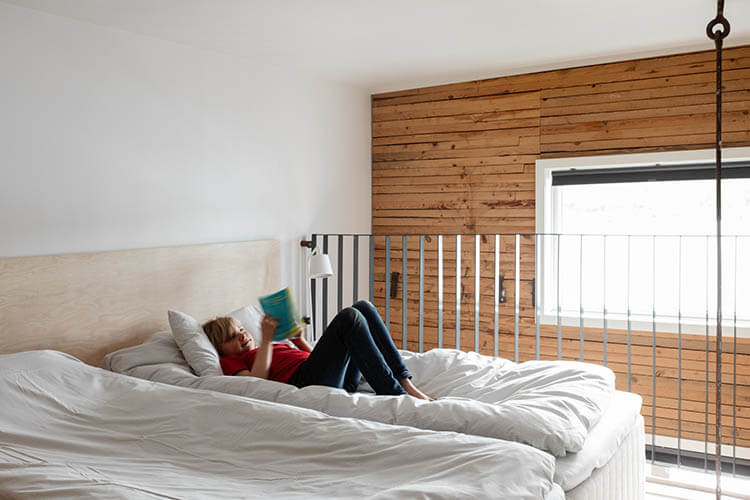 Kind liegt auf einem großen Bett in einem hellen Hotelzimmer mit Holz an der Wand und liest ein Buch