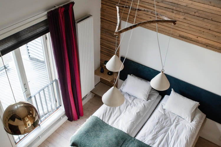 Zwei Einzelbetten mit weißen Bettlaken und Kissen in einem Zimmer mit Holzwand und drei hängenden Lampen