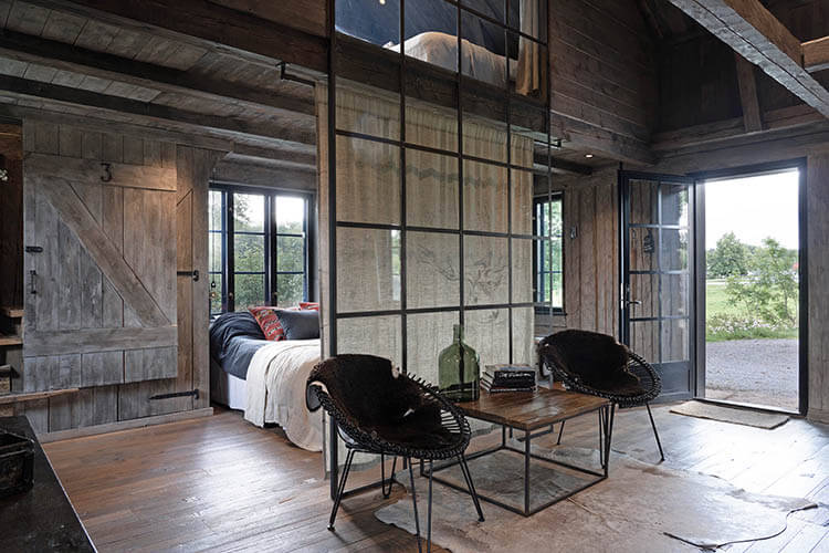 Rustikales Zimmer mit Holzbalken, zwei schwarzen Stühlen, einem Holztisch und offenem Fenster mit Blick ins Grüne