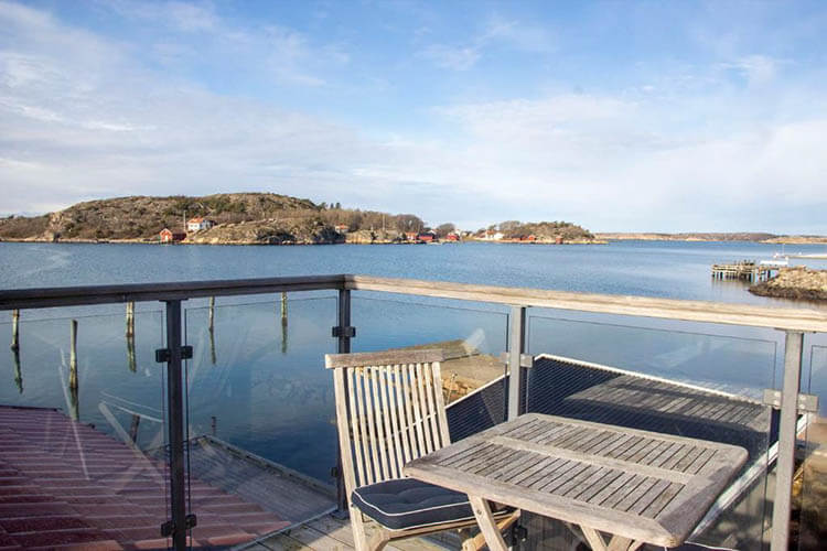 Blick von einem Balkon mit Holztisch und Stühlen auf eine ruhige Schärenlandschaft mit Wasser und kleinen Inseln