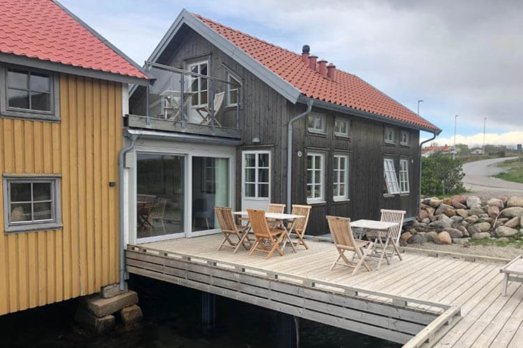 Holzhaus mit rotem Satteldach und Terrasse mit mehreren Holzstühlen und -tischen am Wasser