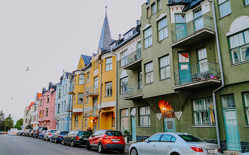 Reihe bunter mehrstöckiger Wohnhäuser mit Balkonen und parkenden Autos in einer ruhigen Straße.