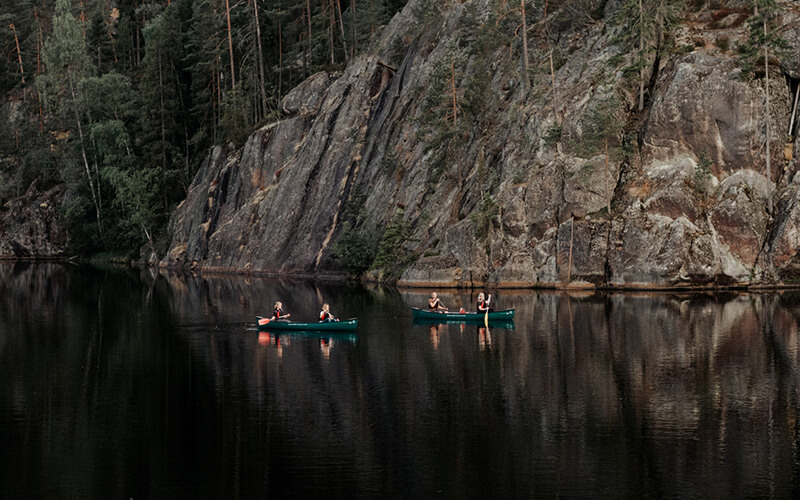 Zwei Kanus mit jeweils zwei Personen auf ruhigem Wasser vor steiler Felswand und Wald.