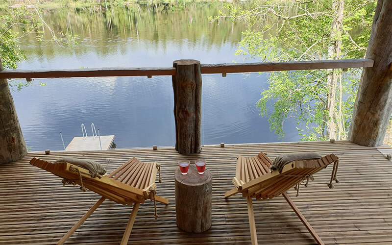 Zwei Holzstühle mit Kissen auf einer Veranda mit Blick auf einen See und einen Steg.