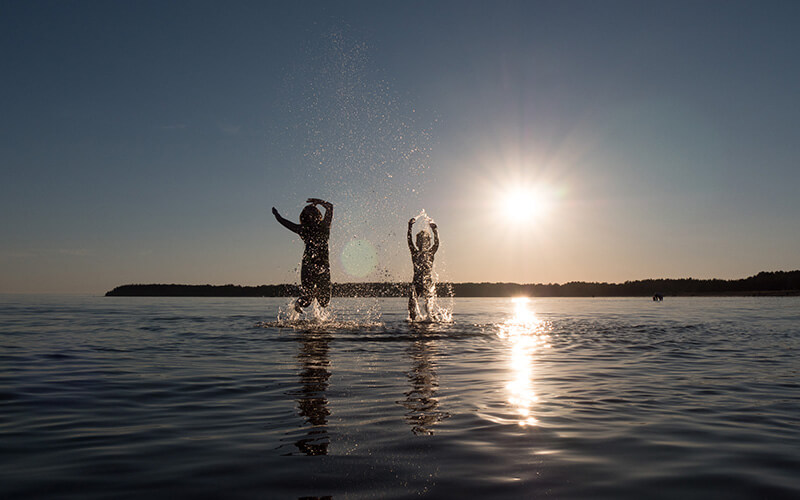 Zwei Personen springen im Wasser bei Sonnenuntergang und spritzen Wasser hoch.