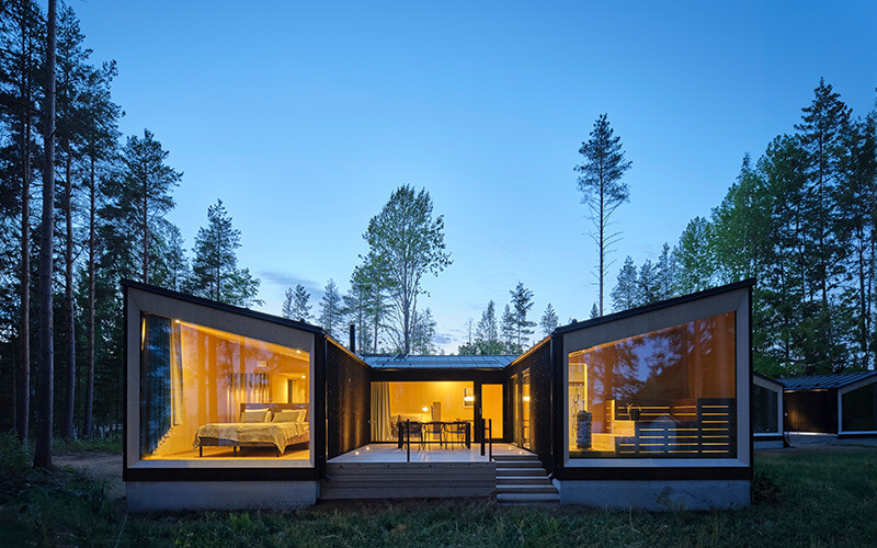 Modernes Haus mit großen bodentiefen Fenstern in einem Wald bei Dämmerung.