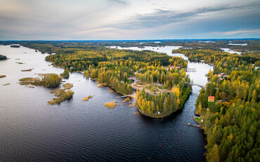 Luftaufnahme eines weitläufigen Seengebiets mit bewaldeten Inseln und Uferbereichen unter bewölktem Himmel.