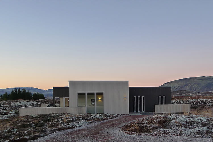 Modernes, kubisches Ferienhaus in karger Landschaft mit Bergen im Hintergrund bei Dämmerung