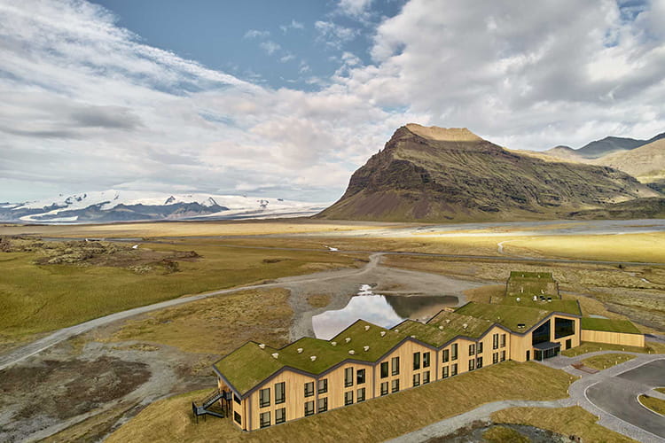 Hotelgebäude mit begrüntem Dach in einer weiten, kargen Landschaft vor einem markanten Berg und Gletscher im Hintergrund