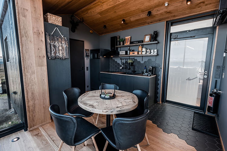 Kleine moderne Küche mit schwarzer Hexagonfliesenrückwand, schwarzer Küchenzeile und rundem Holztisch mit vier schwarzen Stühlen