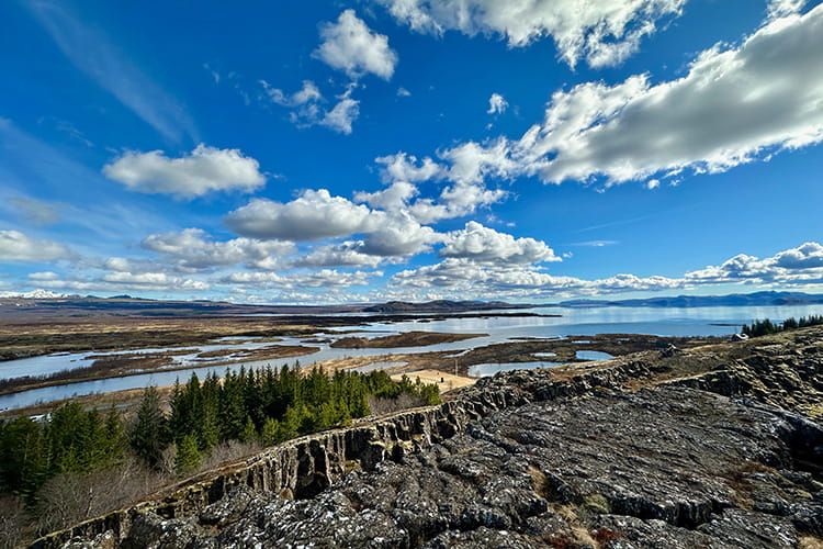 Luftaufnahme einer felsigen Landschaft mit Nadelwald, Flussarmen und bewölktem Himmel