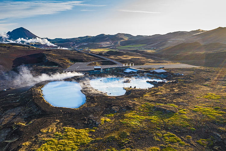 Landschaft mit dampfenden geothermalen Becken und Gebäuden in einer kargen, hügeligen Umgebung