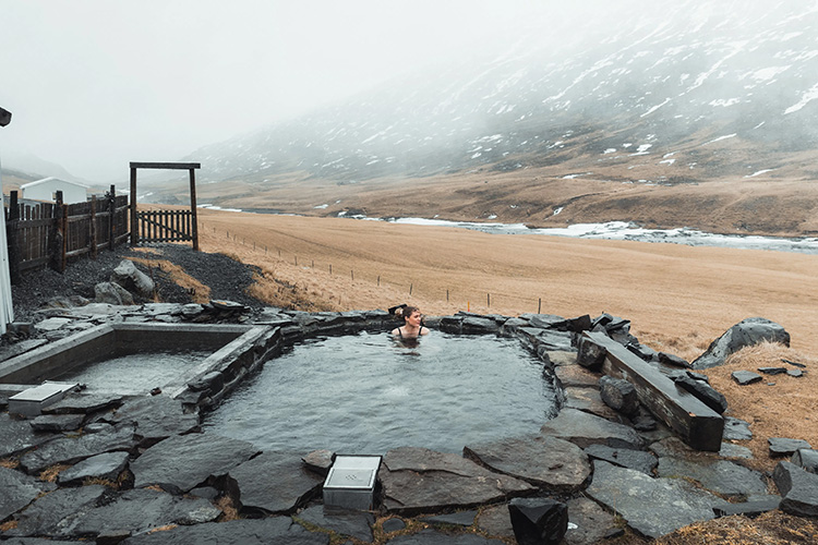 Frau sitzt in einem Pool vor einer nebligen Berglandschaft.