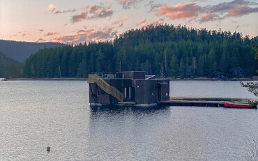 Ein Holzfloß auf einem See. Bäume und pinker Himmel im Hintergrund.
