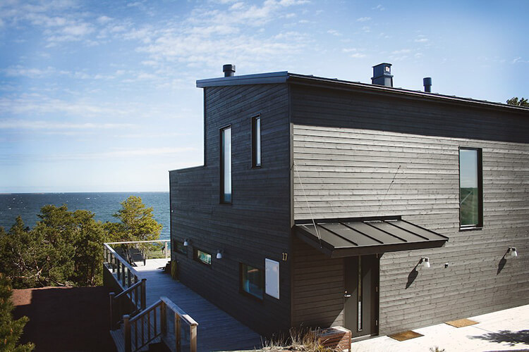 Modernes, zweistöckiges Holzhaus mit dunkler Fassade und Meerblick im Hintergrund