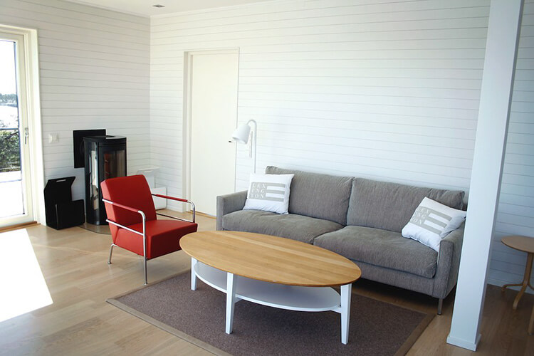 Wohnzimmer mit grauem Sofa, rotem Sessel, ovalem Holztisch und weißer Wandverkleidung