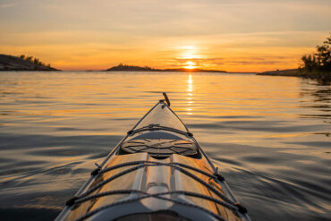 Vorderer Teil eines Kajaks auf ruhigem Wasser bei Sonnenuntergang mit Inseln am Horizont