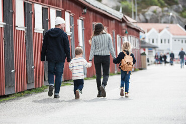 Familie mit zwei Kindern geht an einer Reihe roter Holzhäuser entlang.
