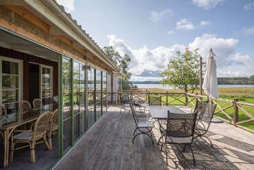 Holzterrasse mit Sonnenschirm, Tisch und Stühlen mit Blick zum See und der grünen Wiese.