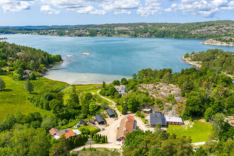 Luftaufnahme einer kleinen Siedlung mit roten Häusern m Wasser umgeben von grünen Wiesen und bewaldeten Hügeln.