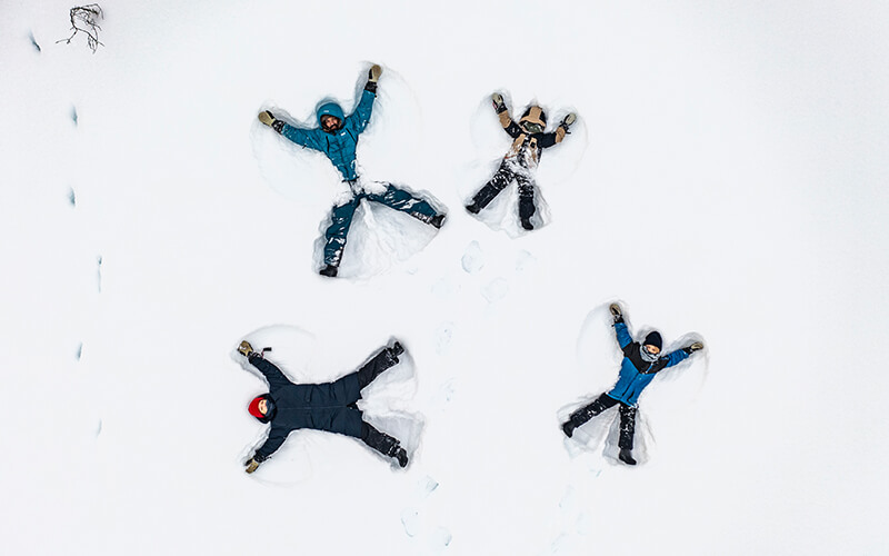 Vier Personen liegen mit ausgestreckten Armen und Beinen im Schnee und machen Schneeengel aus der Vogelperspektive