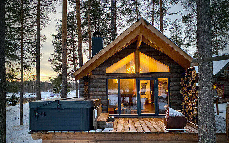 Eine Terrasse von einer Blockhütte mit einem Jacuzzi. Im Hintergrund sind Bäume.