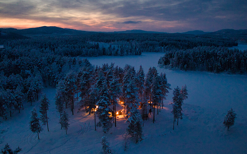 Eine beleuchtete Häuseransammlung in einer dunklen, weiten Winterlandschaft.