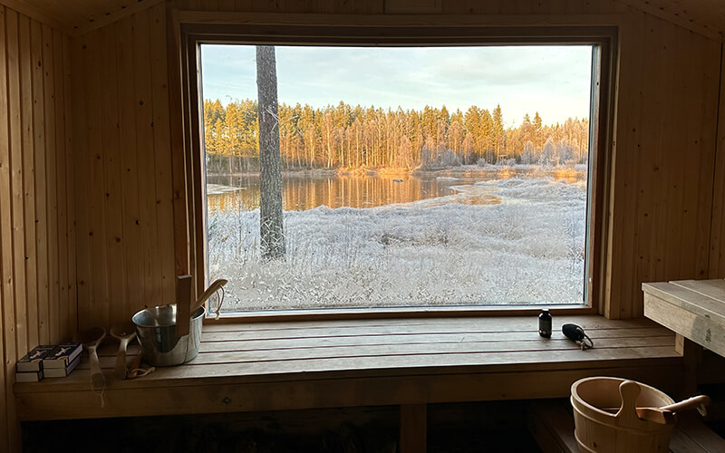 Blick aus einer Sauna durch ein großes Fenster auf eine eisige Landschaft.