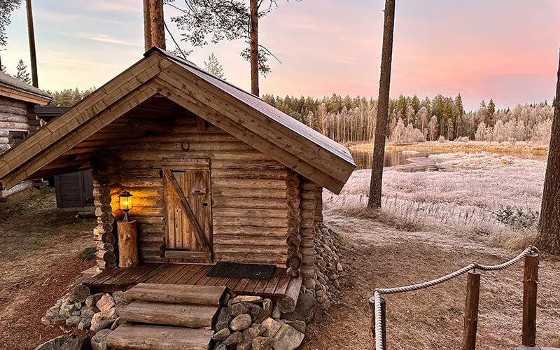 Eine kleine Blockhütte in einer Waldlandschaft, die mit Raureif überzogen ist.