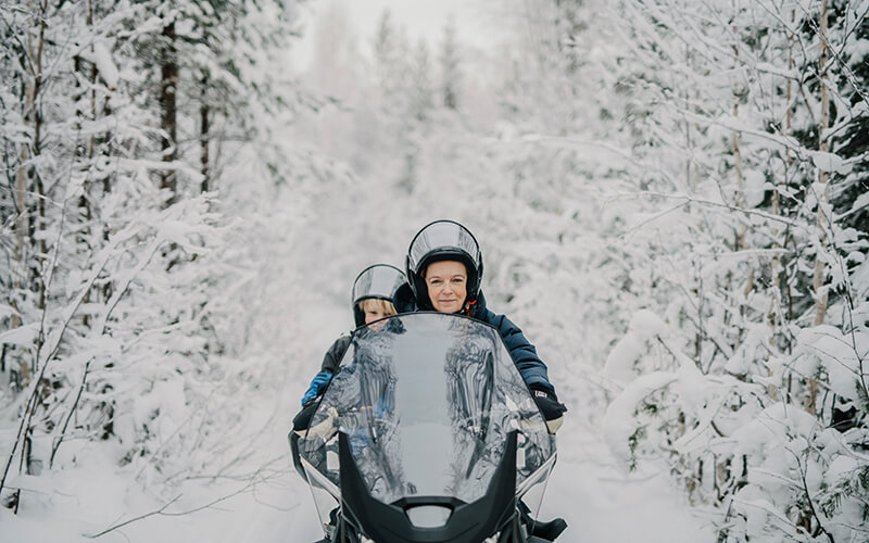 Eine erwachsene Person und ein Kind von vorne auf einem Schneemobil.