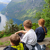 Kinder sitzen an einer Bergkante und schauen auf einen Fjord.