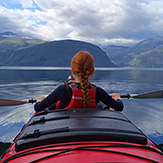 Junges Mädchen im Kajak auf einem Fjord von hinten, stilles Wasser. 