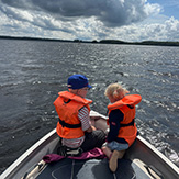 Zwei Kinder in Schwimmwesten auf einem Boot. 