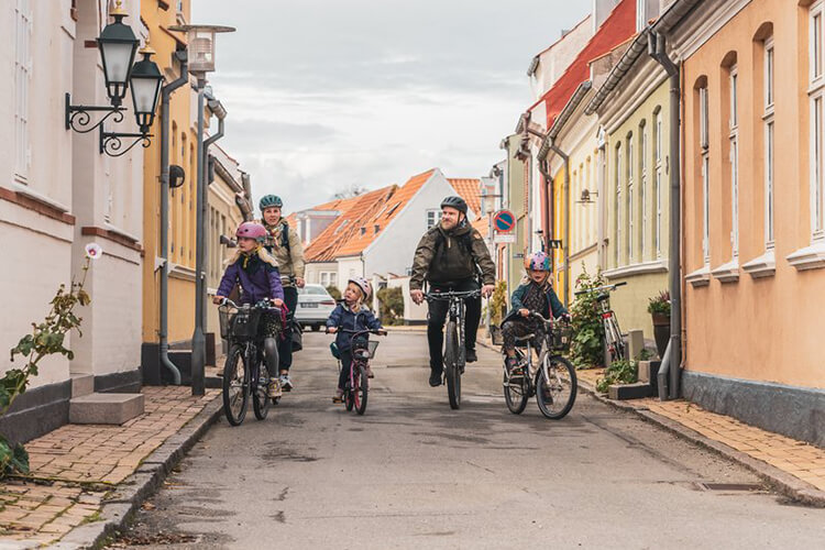 Eine Familie fährt mit Fahrrädern durch eine Straße mit bunten Häusern.