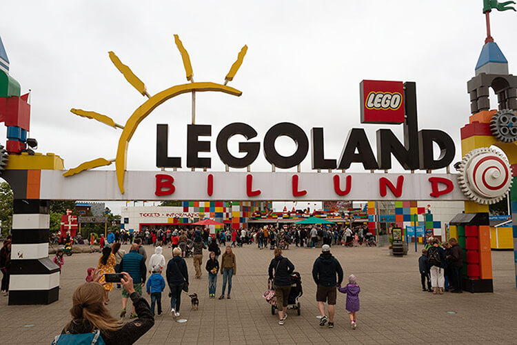 Eingangstor von LEGOLAND Billund mit großem gelbem Sonnenmotiv und vielen Besuchern davor.